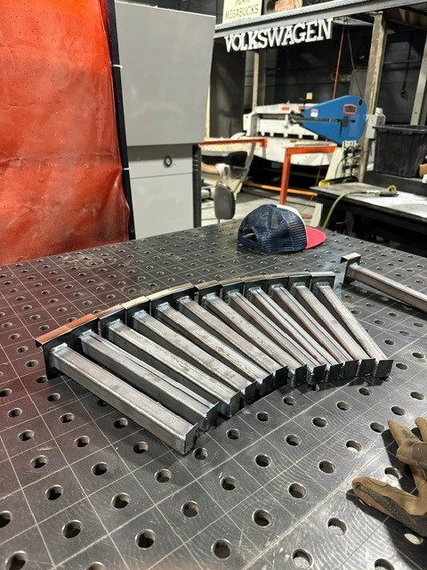 Row of identical steel brackets tacked in a curve on a fixture table