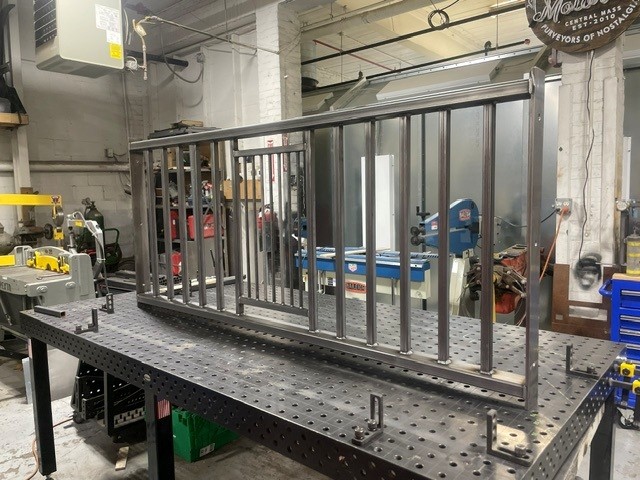 Bare steel stair railing section with vertical balusters clamped on a welding table