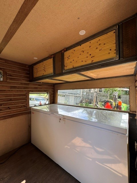 Wood-lined mobile bar trailer interior with a chest cooler and flip-up serving windows