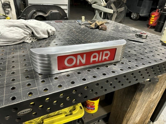Brushed aluminum ON AIR sign with red illuminated face on a welding table
