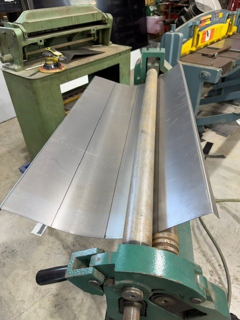 Aluminum sheet being rolled into a curved panel on a slip roll machine