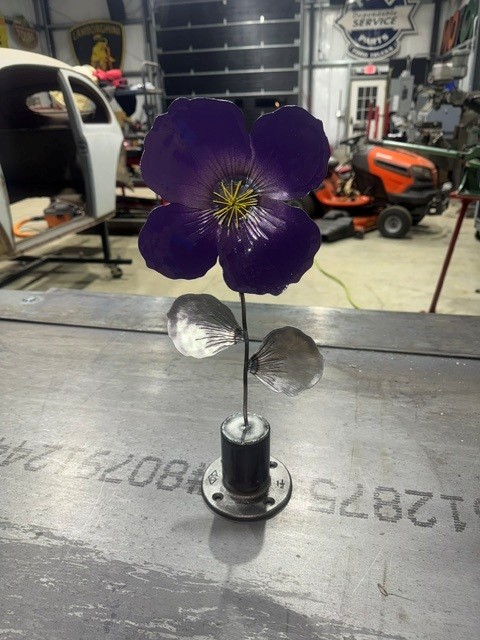 Small steel flower sculpture with purple painted petals on a flanged base